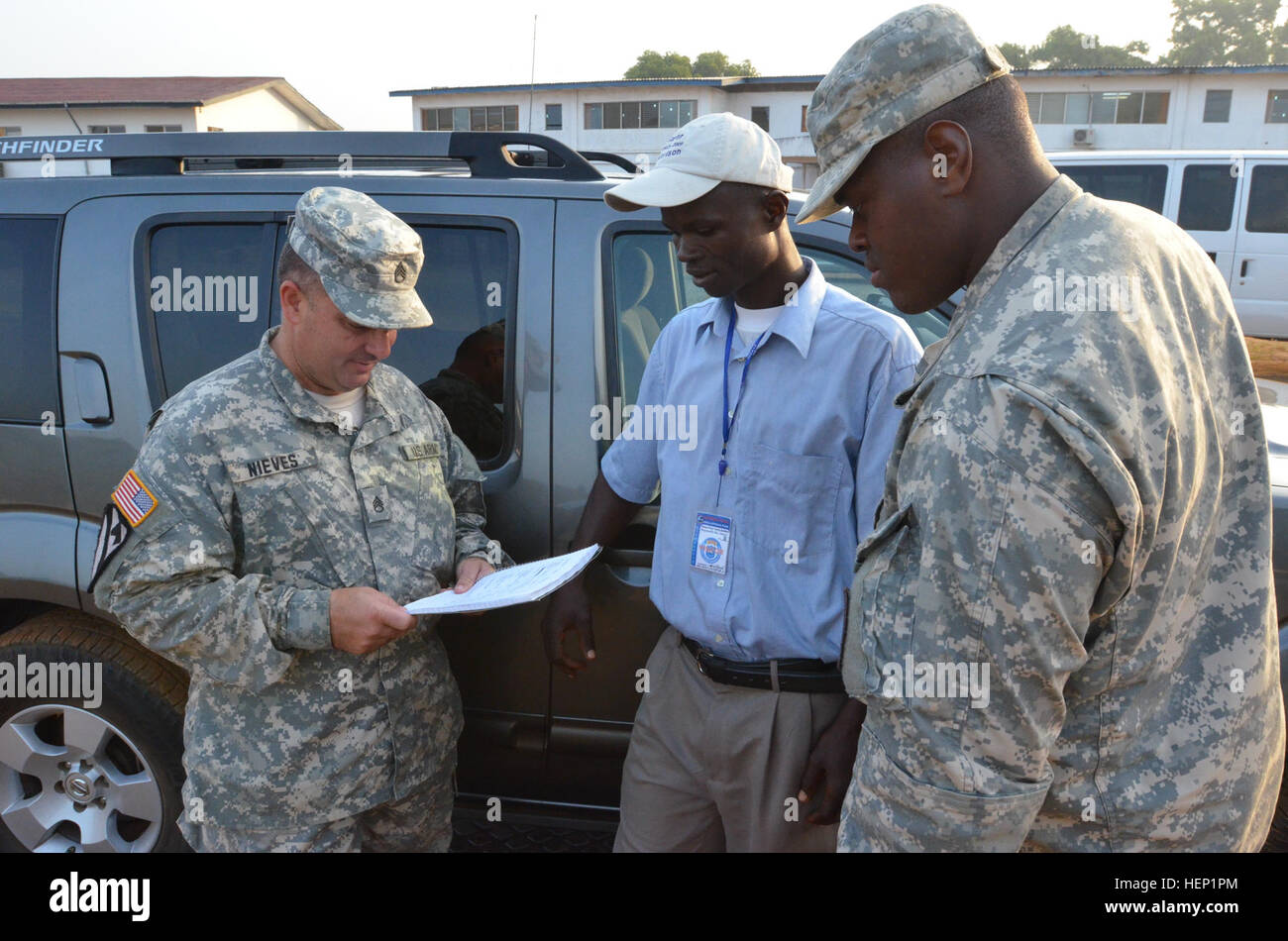 From left, Staff Sgt. Jose Nieves, a Bayamon, Puerto Rico, native and movement noncommissioned officer for Headquarters and Headquarters Company, 36th Engineer Brigade, talks to Haji A. Sheriff, a Liberia, Monrovia native and a driver, about his routes before he goes out on a mission to Buchanan, Liberia, Dec. 27, 2014, from the National Police Training Academy, Paynesville, Liberia, during Operation United Assistance. Spc. Joshua Owens, Chicago native and a movement specialist also with HHC, 36th Engineer Brigade, listens to the conversation. Operation United Assistance is a Department of Def Stock Photo
