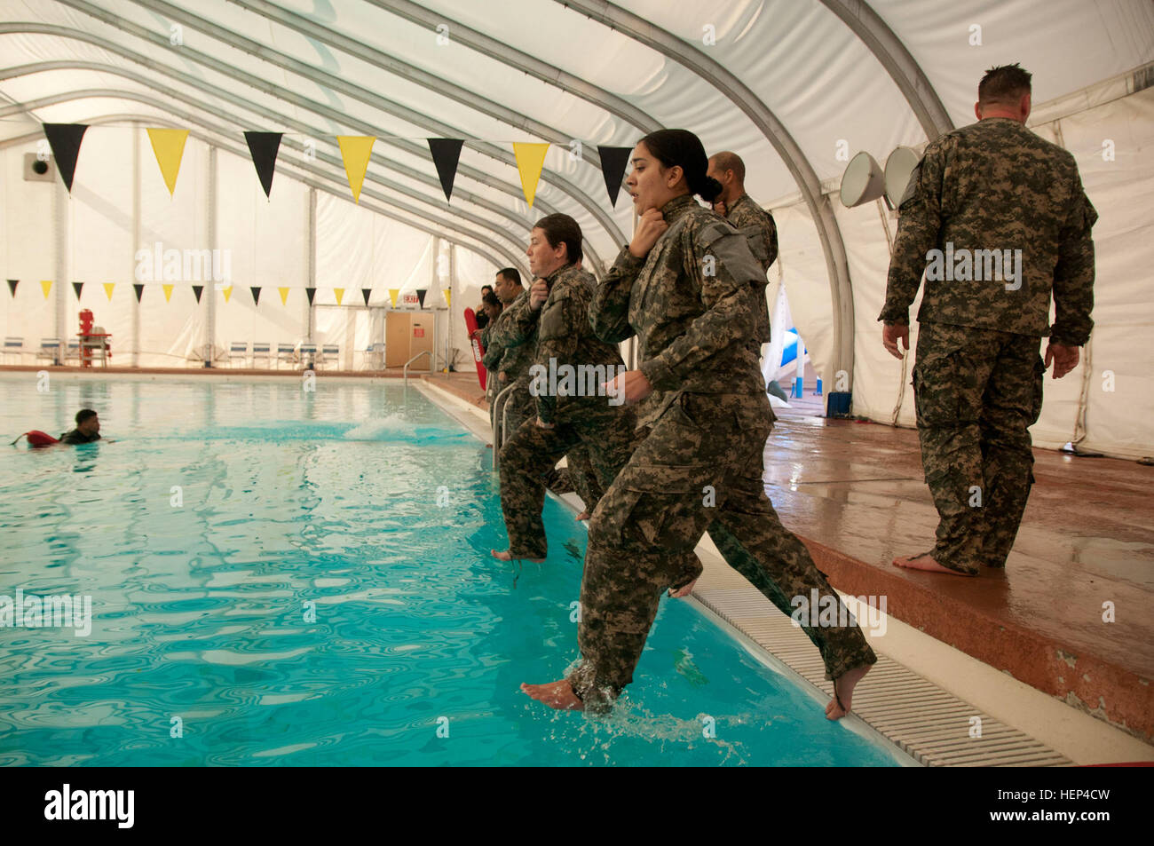 Pfc. Nicholle Salvatierra, a broadcast journalist, and Staff Sgt. Mary Healy, a visual information equipment maintainer, both with the 222nd Broadcast Operations Detachment, jump feet-first into the pool at the drown-proofing training session at Fort Irwin, Calif., Feb. 7, 2015. The 222nd BOD and the 302nd Mobile Public Affairs Detachment participated in drown proofing to prepare their Soldiers for the possibility of survival during an open water emergency. (U.S. Army photo by Sgt. David L. Nye, 204th PAD) Public affairs learns water survival in the desert 150207-A-ZZ999-005 Stock Photo