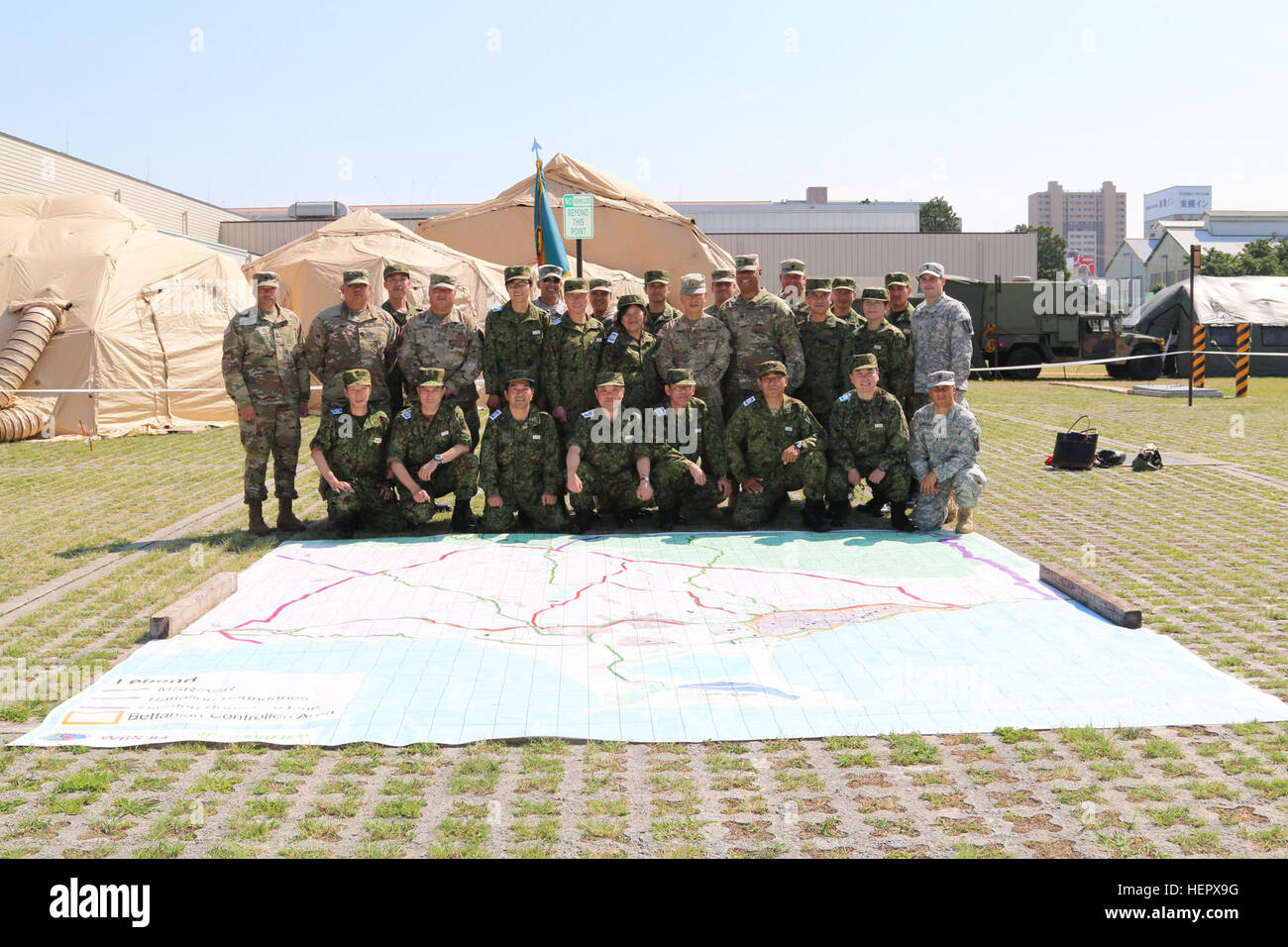 U.S. and Japan Ground Self-Defense Force (JGSDF) service members pose for a photo behind a 30 by 30 feet map outside Sagamihara Depot Mission Training Complex during a visit from Brig. Gen. Stephen K. Curda, Commander, 9th Mission Support Command, and exercise Imua Dawn 2016, Sagamihara, Japan, June 18, 2016.  Imua Dawn 2016 provides opportunities for U.S. and Japanese forces to come together and train for potential real world events, better preparing them in supporting regional populations in all Humanitarian Assistance and Disaster Relief (HADR) and Noncombatant Evacuation Operations (NEO).  Stock Photo