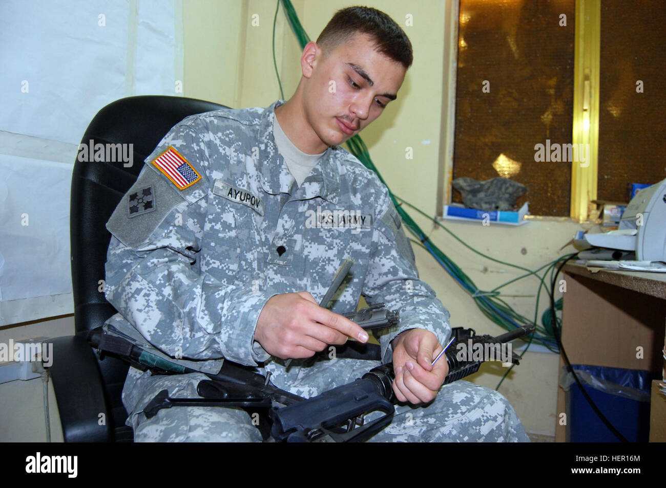 CAMP TAJI, Iraq – Spc. Eynar Ayupov, personnel clerk, Headquarters Support Company, 404th Aviation Support Battalion, Combat Aviation Brigade, 4th Infantry Division, Multi-National Division – Baghdad from Ufa, Russia, cleans his M16A2 rifle while sitting at his desk on Camp Taji Oct. 14. Ayupov was born and raised in Russia and has been in the U.S. Army since November 2006. He is scheduled to become a U.S. citizen while deployed to Iraq.  (U.S. Army photo by Sgt. 1st Class Brent Hunt, CAB PAO, 4th Inf. Div., MND-B) Why I Serve, Russian-born CAB Soldier scheduled for citizenship, enjoys U.S. Ar Stock Photo