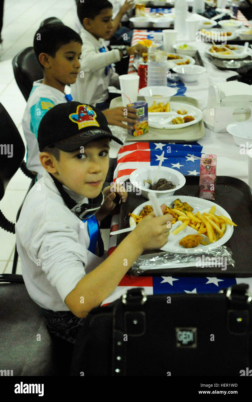 A young Iraqi boy enjoys a hearty meal, Nov. 12, at the Raider Cafe Dining Facility at Forward Operating Base Falcon, Iraq. Soldiers from the 1st Brigade Combat Team, 4th Infantry Division, Multi-National Division - Baghdad, facilitated a video teleconference between approximately 20 Iraqi children from the al Khartoum primary school and more than 40 students from the Nolanville Elementary School in Central Texas. The cultural exchange is part of a School Partnership Program, which currently involves 31 Iraqi and American schools. Cultural borders extended during Iraqi, American video teleconf Stock Photo