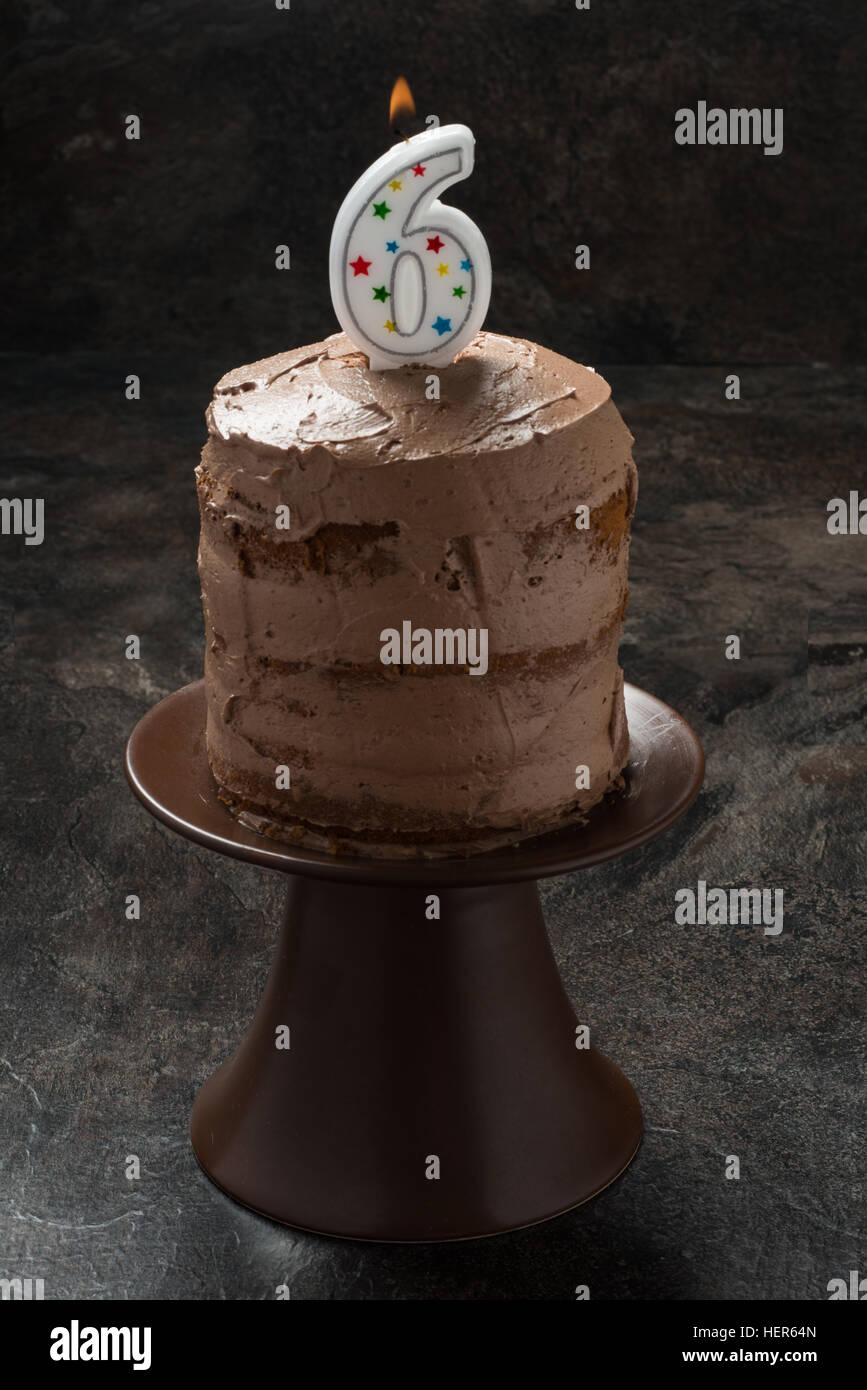 Three layer chocolate cake with icing and candle on brown background