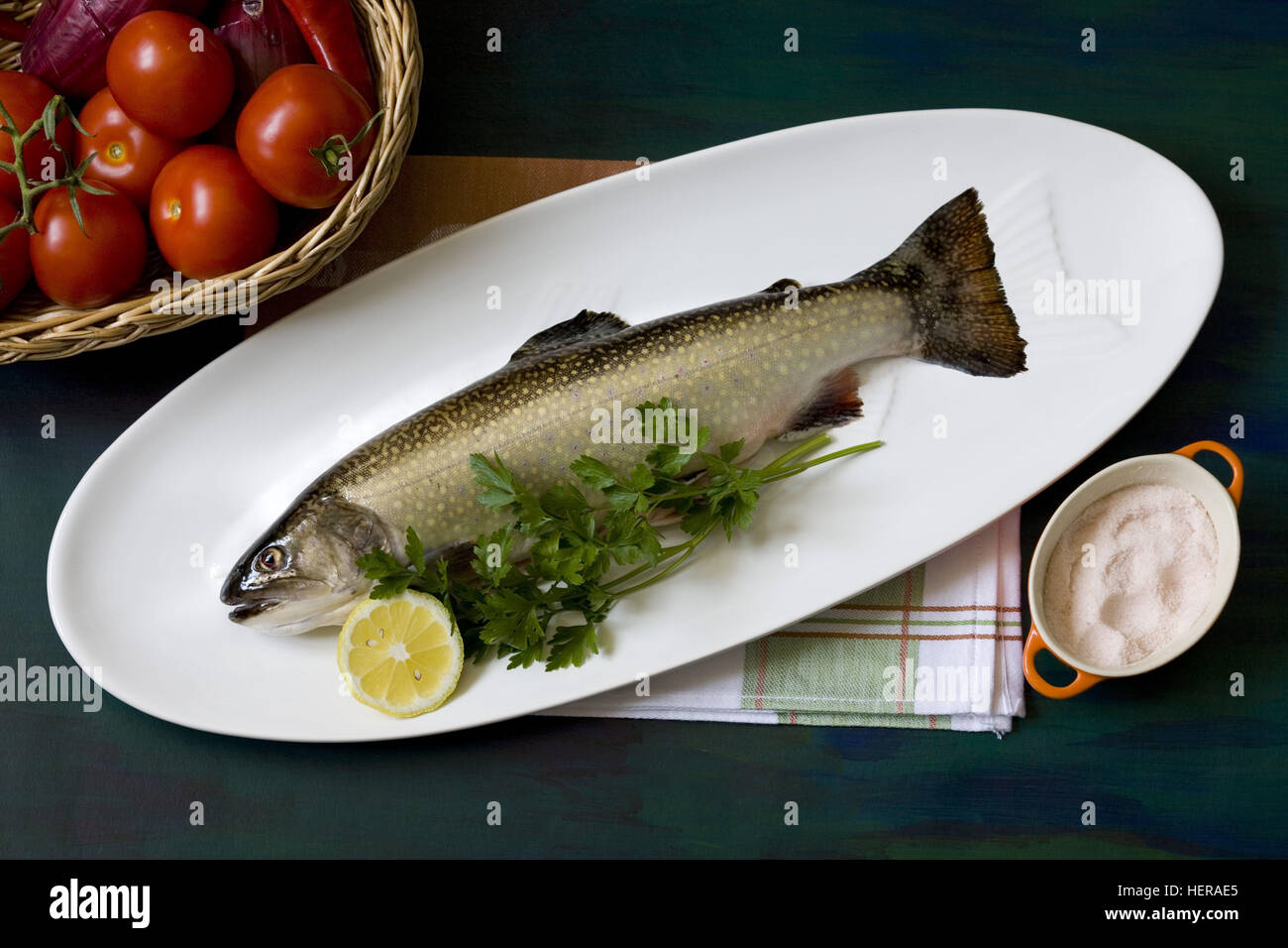 Bachsaibling auf Fischteller mit Gemüsekorb und Salz Stock Photo