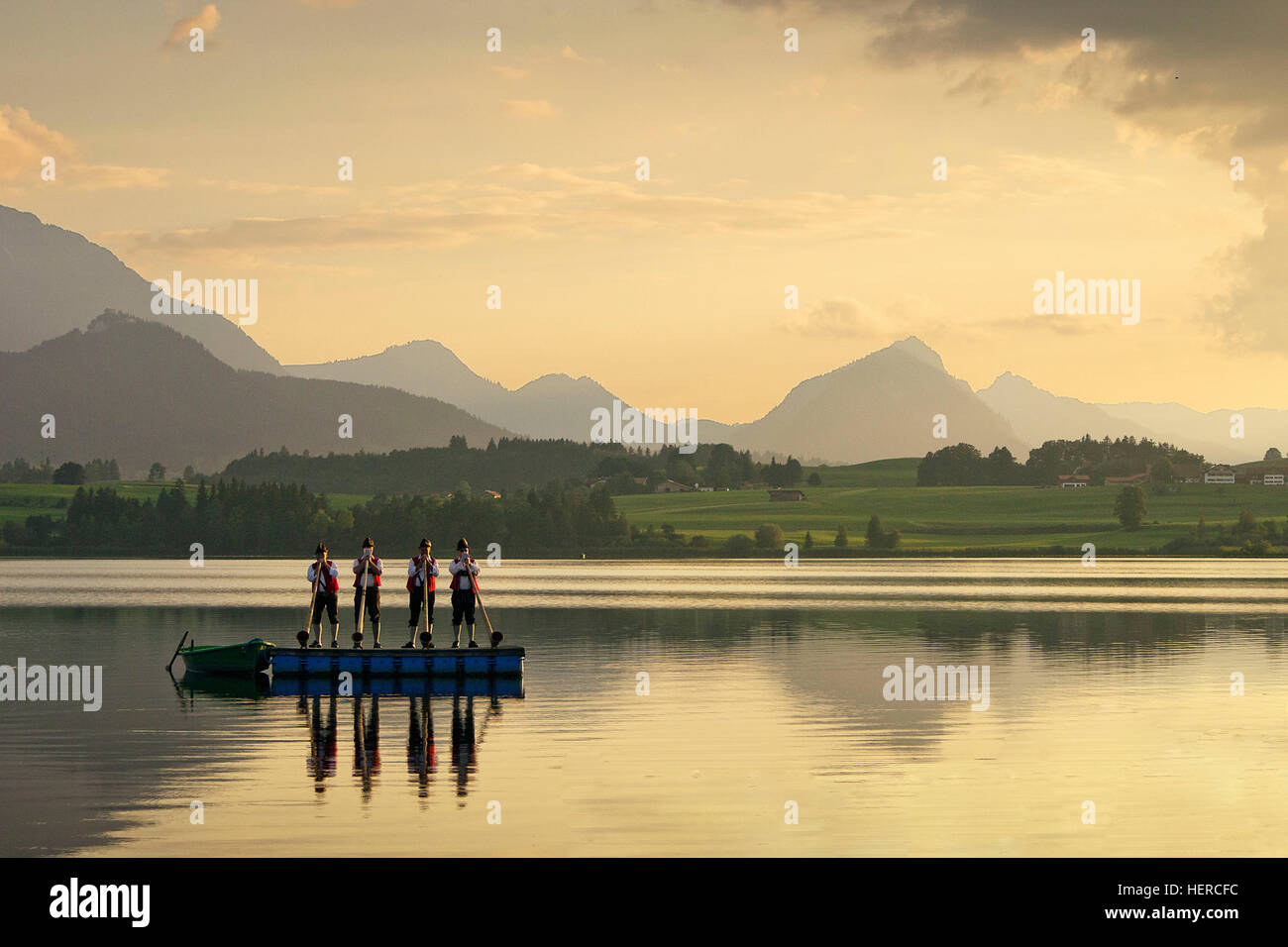 The alpenhorn blowers are reflecting at sundown in the summery Hopfensee lake, Alpine panorama in background Stock Photo