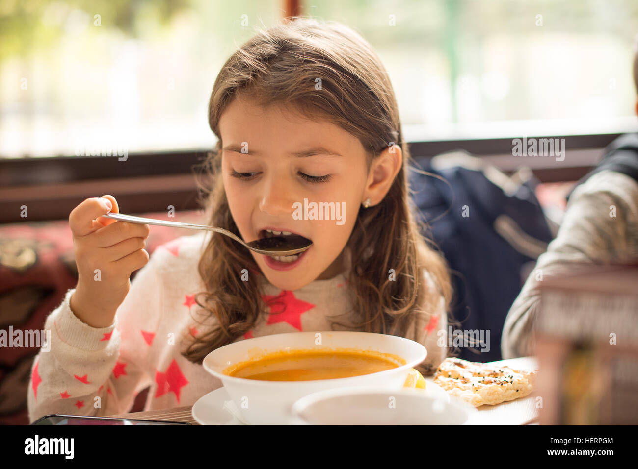 Girl eating soup while looking at her mobile phone Stock Photo