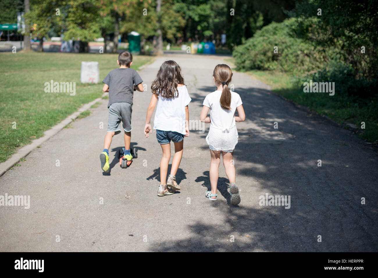 Three children walking along footpath in park Stock Photo
