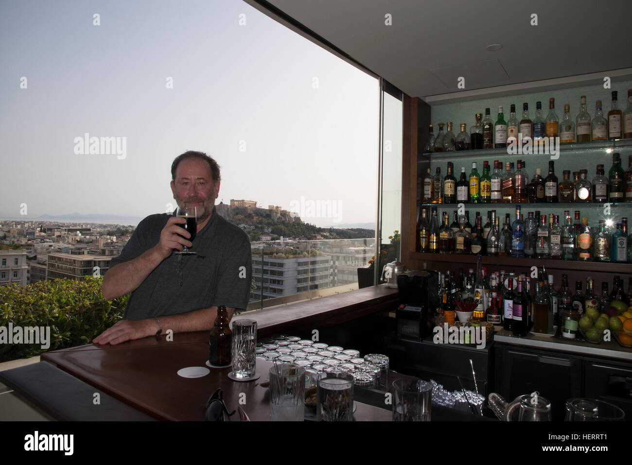 Man sits at rooftop bar In Athens drinking a beer, behind is the Acropolis Stock Photo