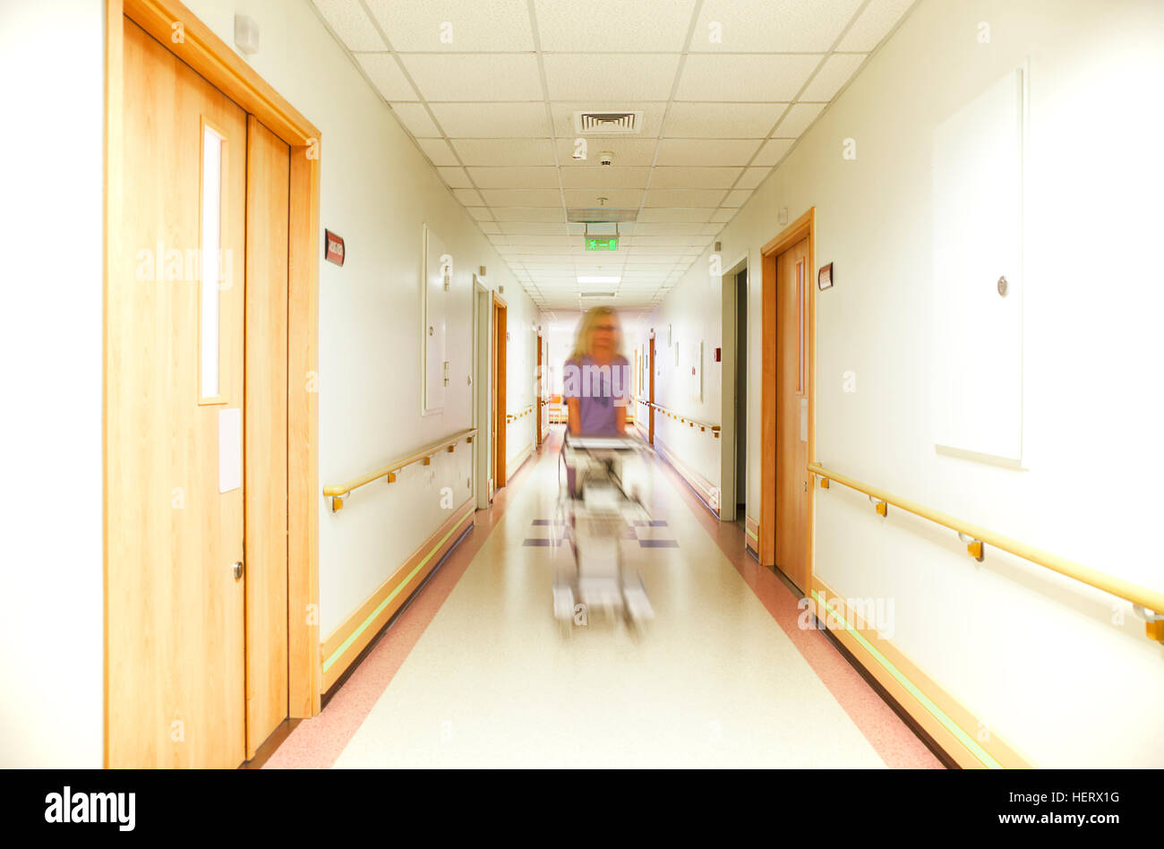 A blurred figure of nurse, coming down a well lit hospital corridor, pushing equipment. Stock Photo