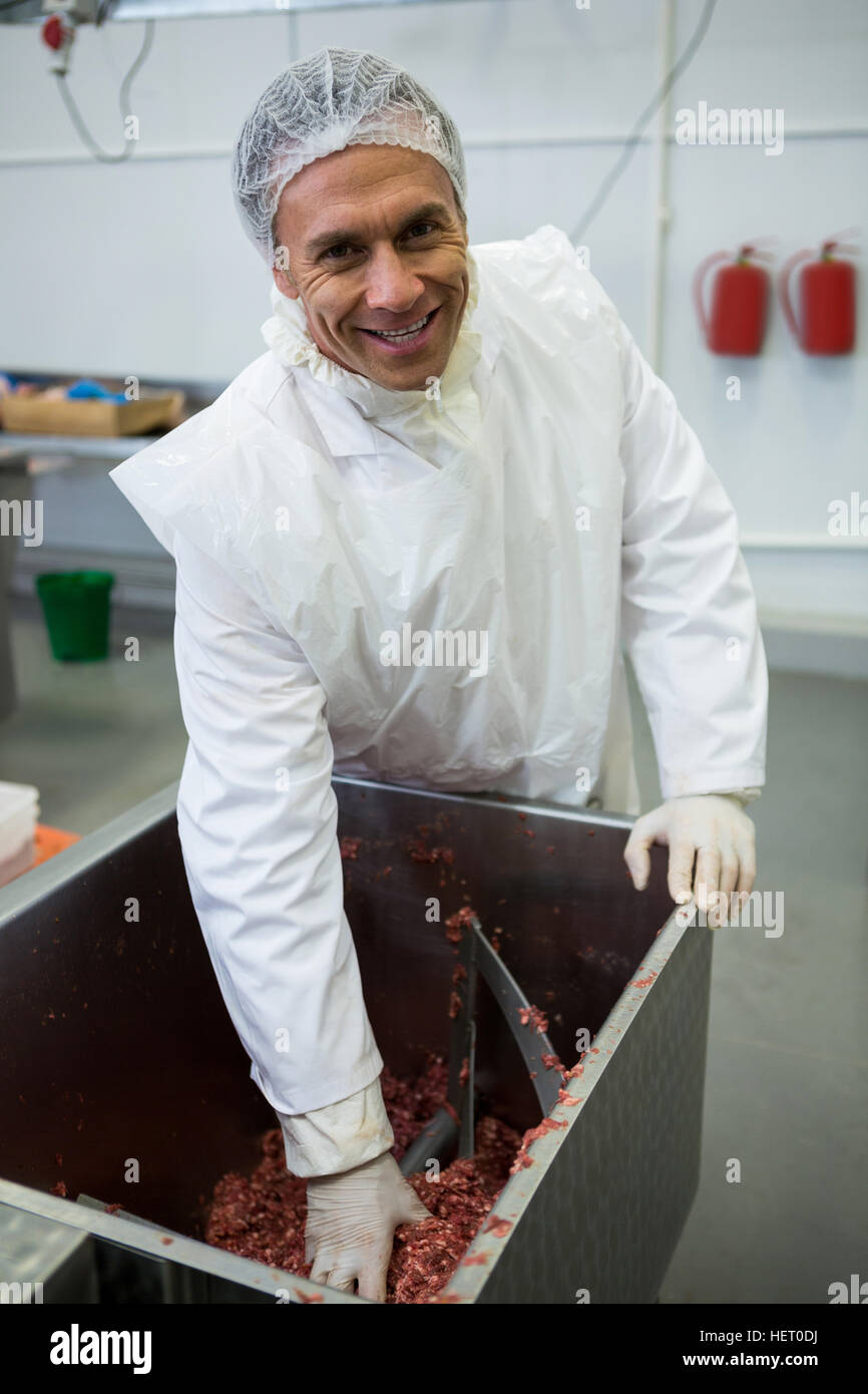 Portrait of butcher removing minced meat from machine at meat factory
