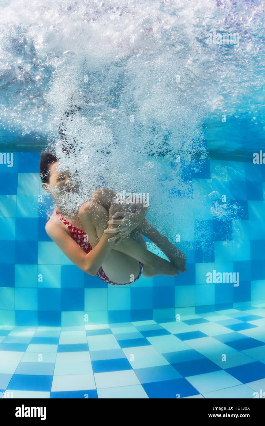 Funny face portrait of girl swimming and diving in blue pool with fun - jumping deep down underwater with splashes and foam. Stock Photo