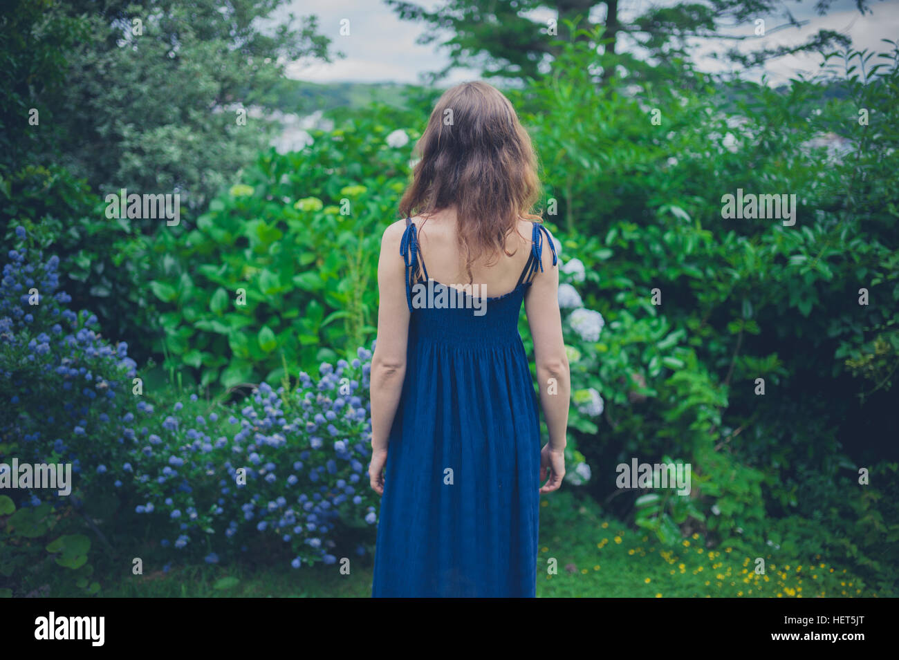A young woman wearing a blue dress is standing by some flowers in a ...