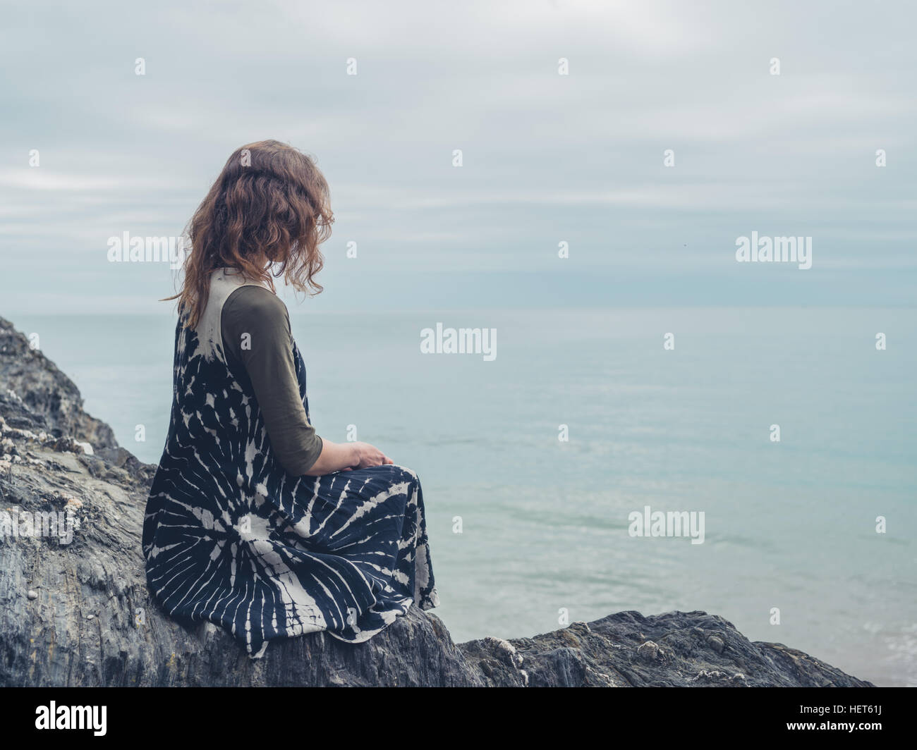 A young woman is sitting on some rocks by the sea Stock Photo - Alamy
