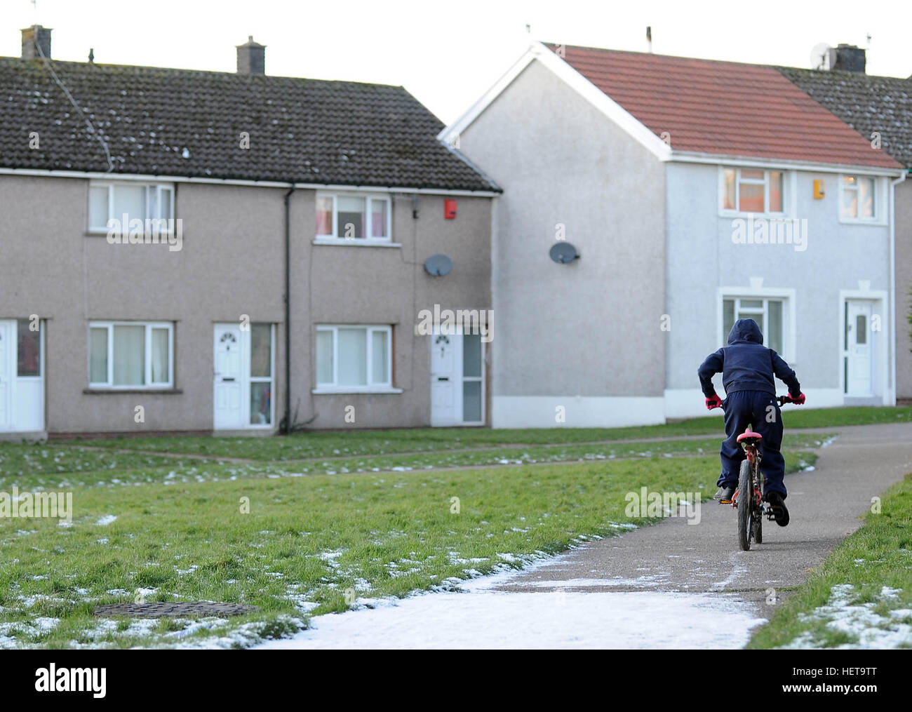 A boy cycles on a snow covered path on the Gurnos Council housing estate in Merthyr Tydfil, South Wales, UK. Stock Photo