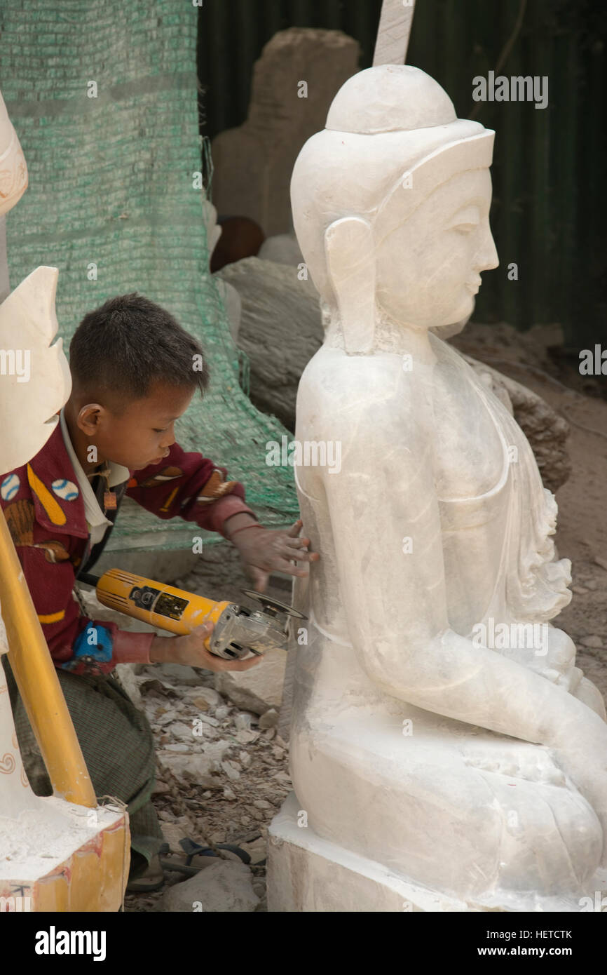 ASIA, MYANMAR (BURMA), Mandalay, boy using an electric sanding machine  on a statue of Buddha in outdoor factory Stock Photo