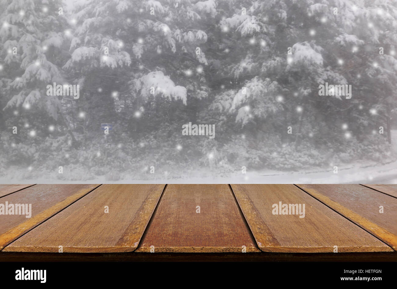 Blurred snowing in pine forest through glass window background with wood table. Stock Photo