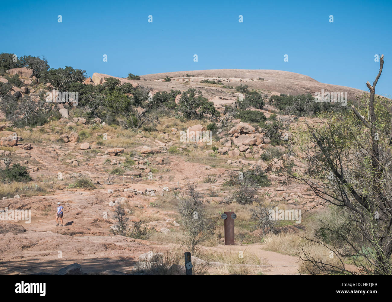 Lone hiker descends Summit Trail to top of Enchanted Rock. Trail marker at bottom of image. Stock Photo