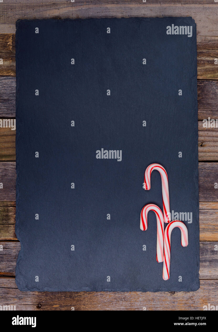 Holiday striped candy canes on dark stone board and wooden background. Top view, flat lay. Stock Photo