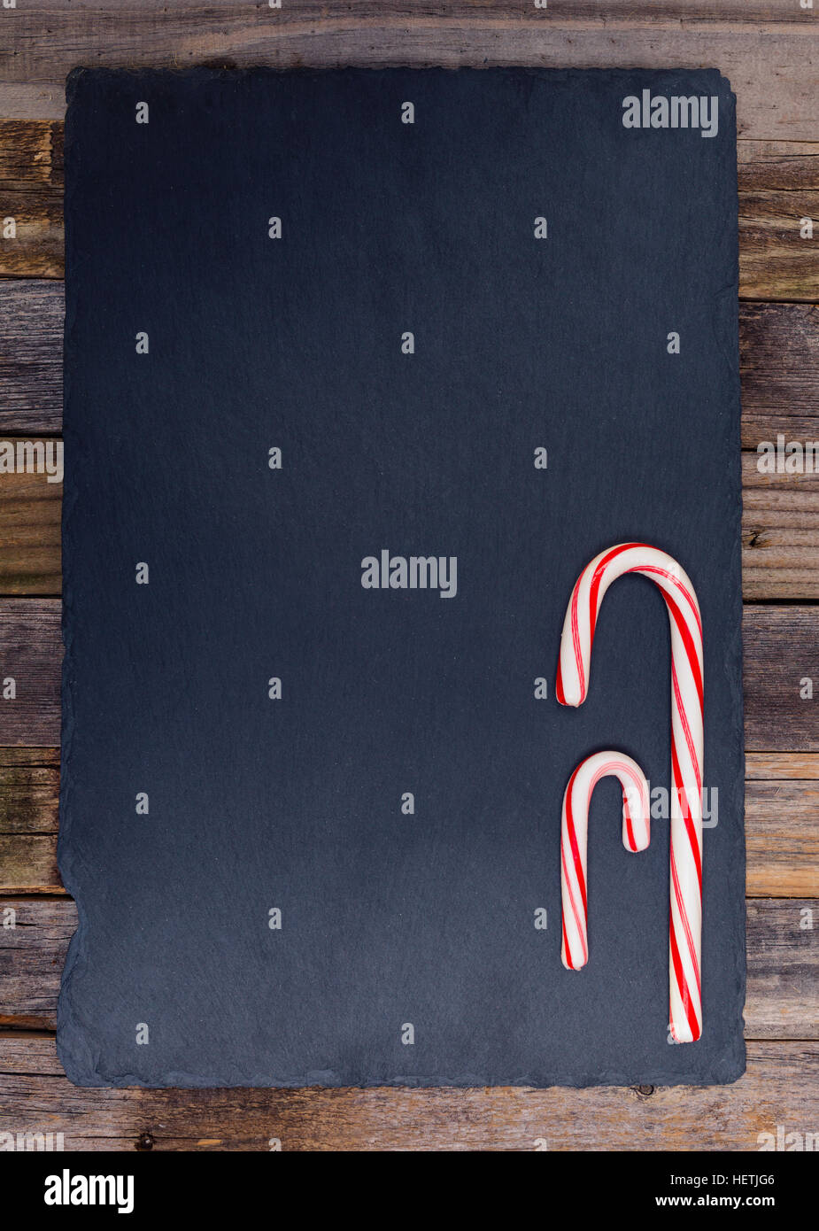 Holiday striped candy canes on dark stone board and wooden background. Top view, flat lay. Stock Photo