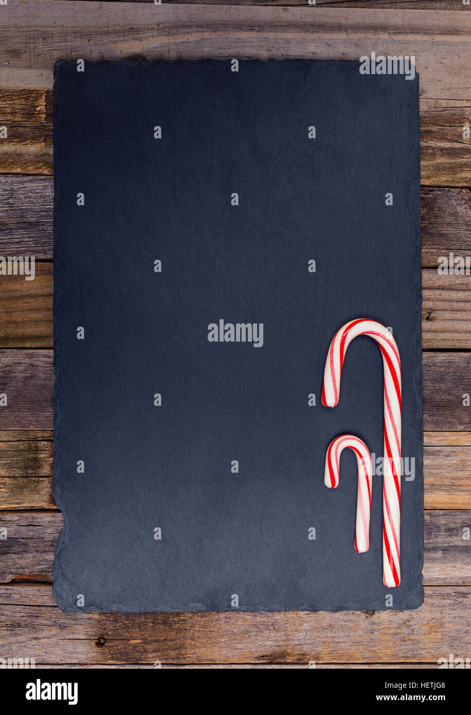 Two holiday striped candy canes on dark stone board and wooden background. Top view, flat lay. Stock Photo