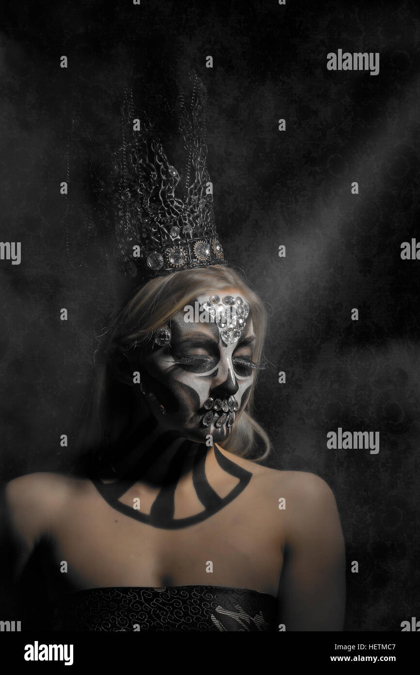 Black and white Day of the Dead creative makeup in candy skull style with gothic crown, sitting in a ray of light Stock Photo