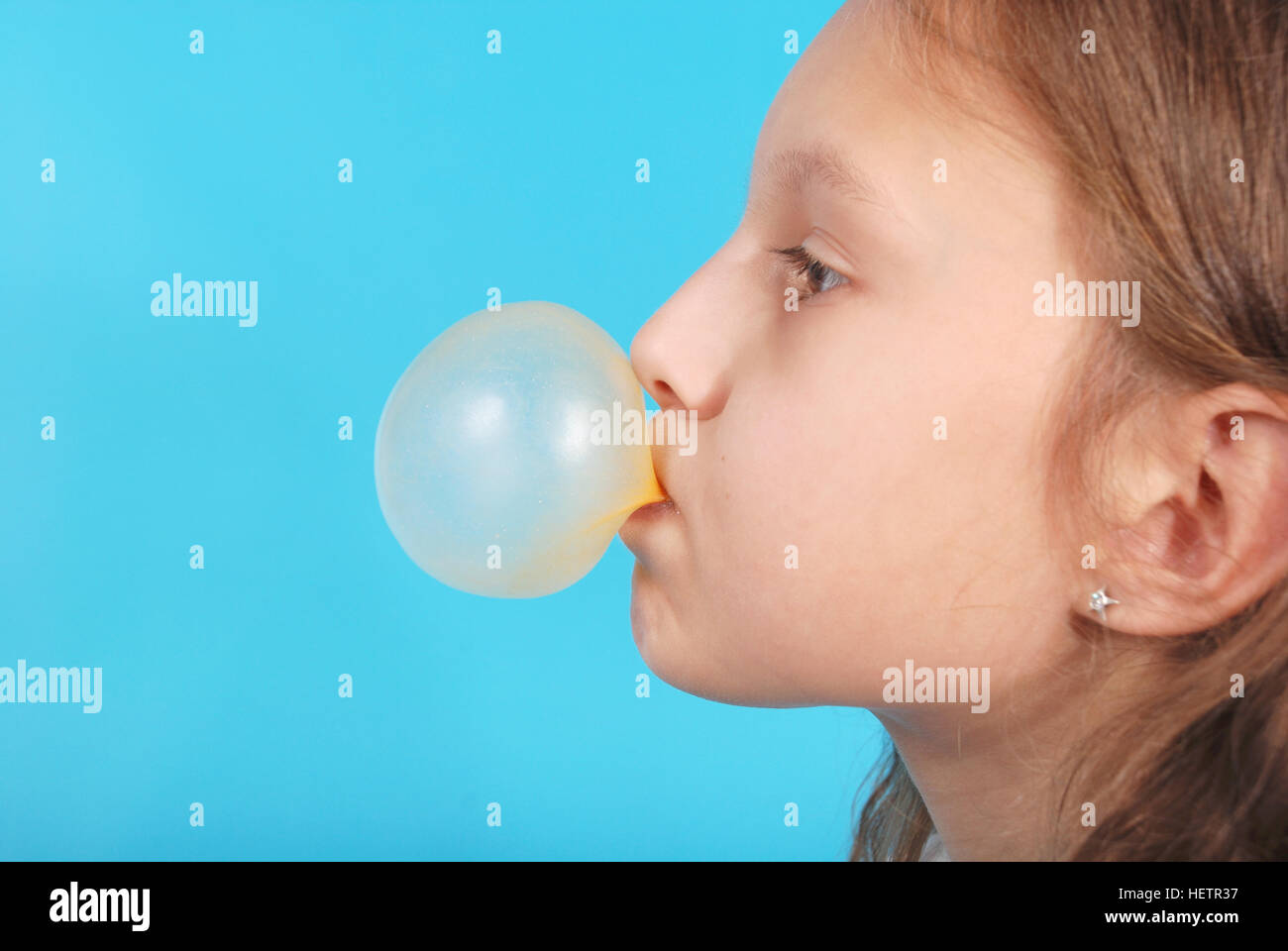 Young girl doing bubble with chewing gum blue background Stock Photo