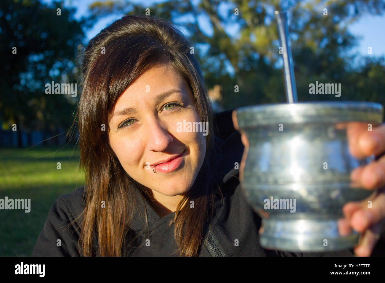 Young woman at the park smiling and drinking mate Stock Photo