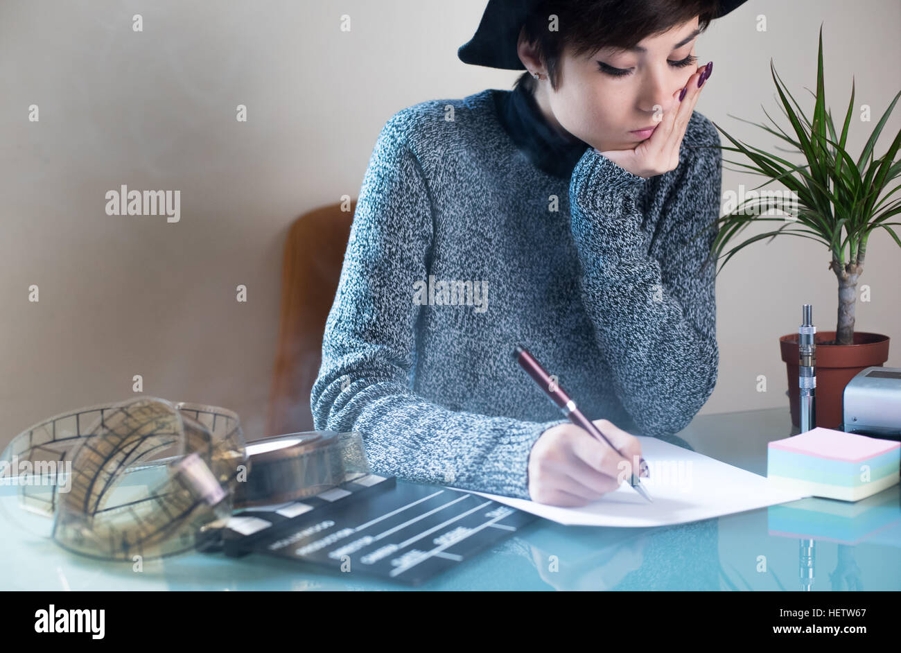 Young pretty woman writing on desktop with movie objects, clapper and filmstrip, with cigarette smoke in the air Stock Photo