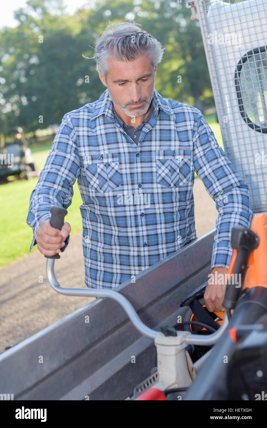 Man loading strimmer into work vehicle Stock Photo
