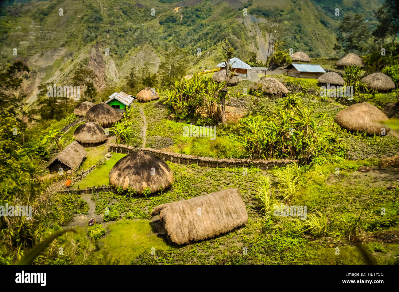 Photo of traditional village houses with straw roofs in village surrounded by high mountains in Dani circuit near Wamena, Papua, Indonesia. Stock Photo