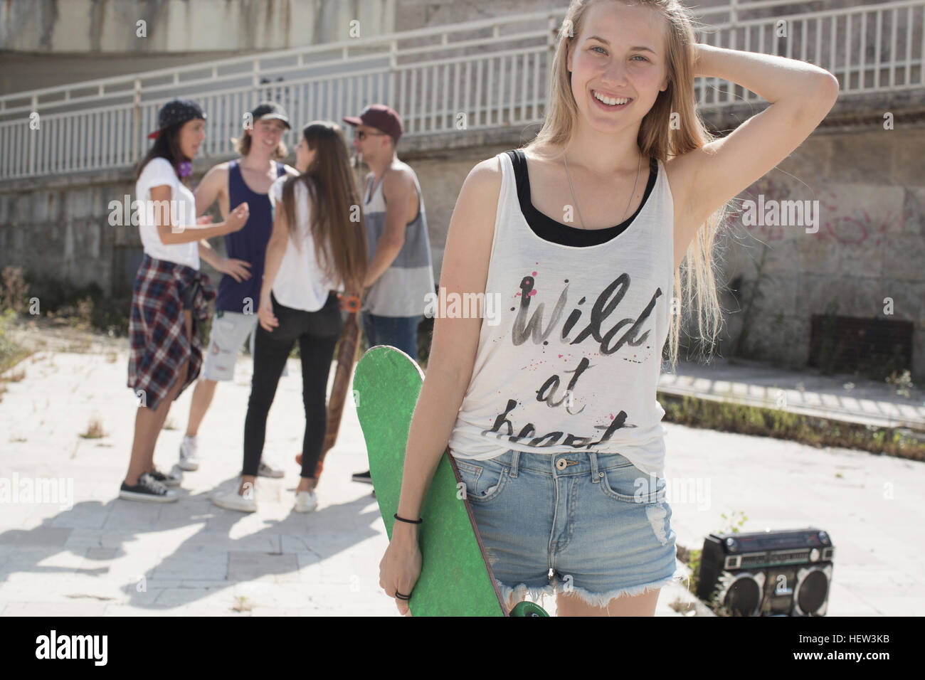 Skateboarder in tank top with wild at heart slogan, friends in background Stock Photo