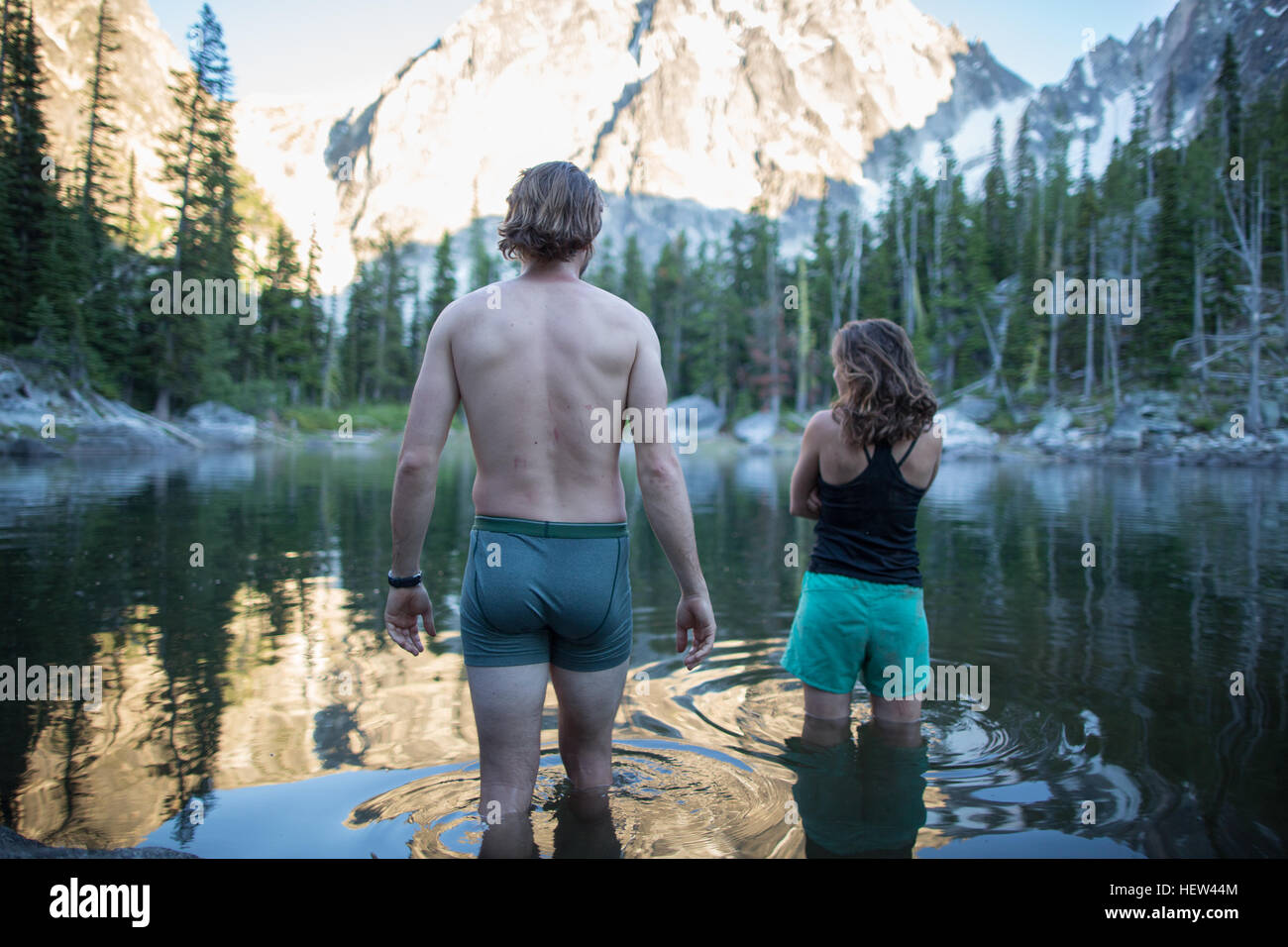 Young man and woman standing in lake, rear view, The Enchantments, Alpine Lakes Wilderness, Washington, USA Stock Photo