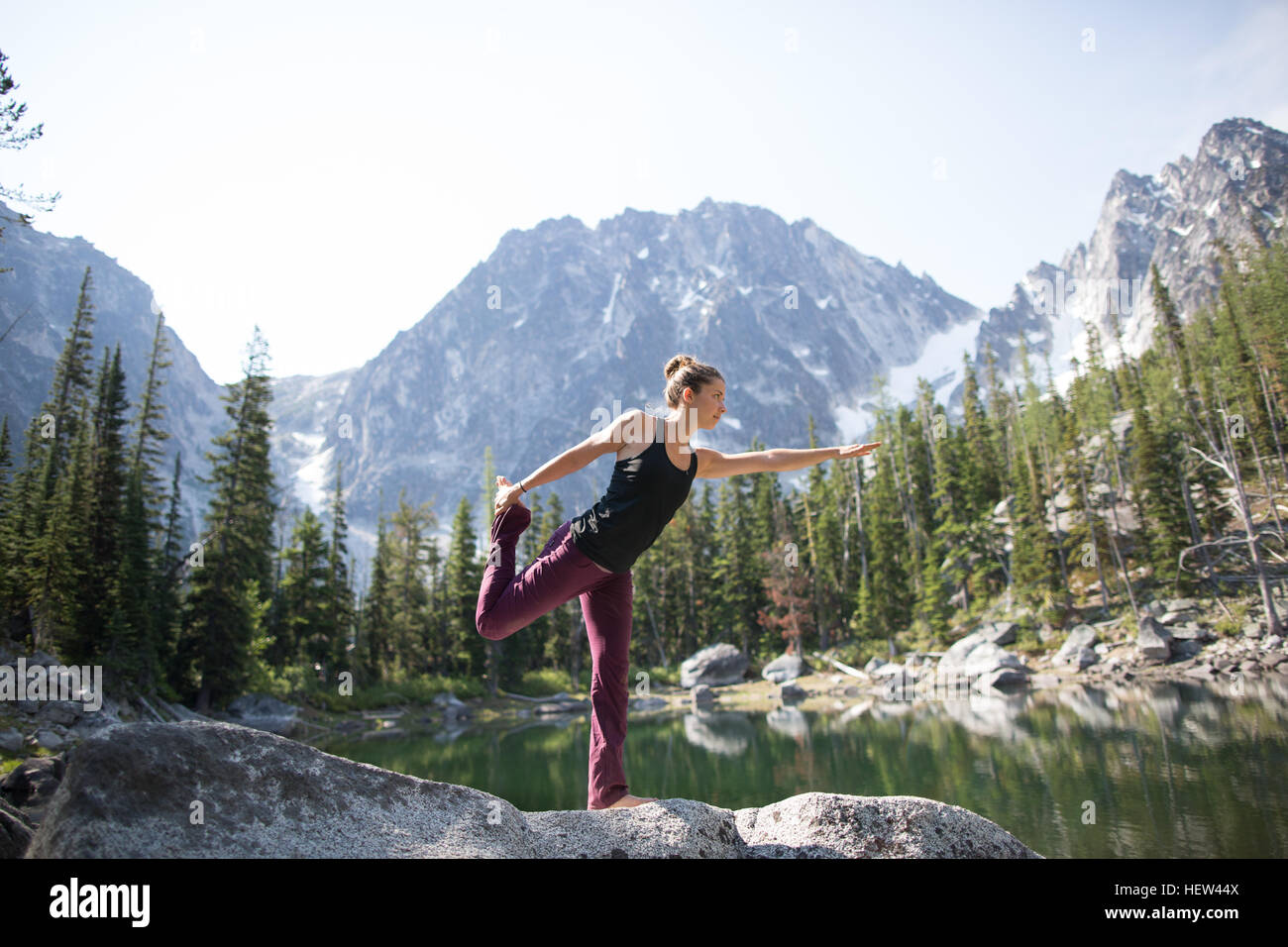 Young woman standing on rock beside lake, in yoga pose, The Enchantments, Alpine Lakes Wilderness, Washington, USA Stock Photo