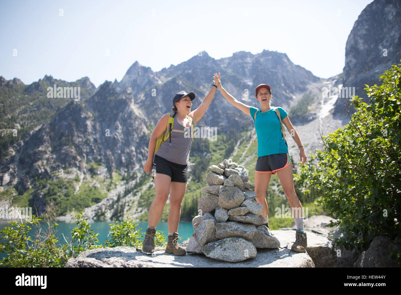 Two young women standing by pile of rocks, giving high-five, The Enchantments, Alpine Lakes Wilderness, Washington, USA Stock Photo
