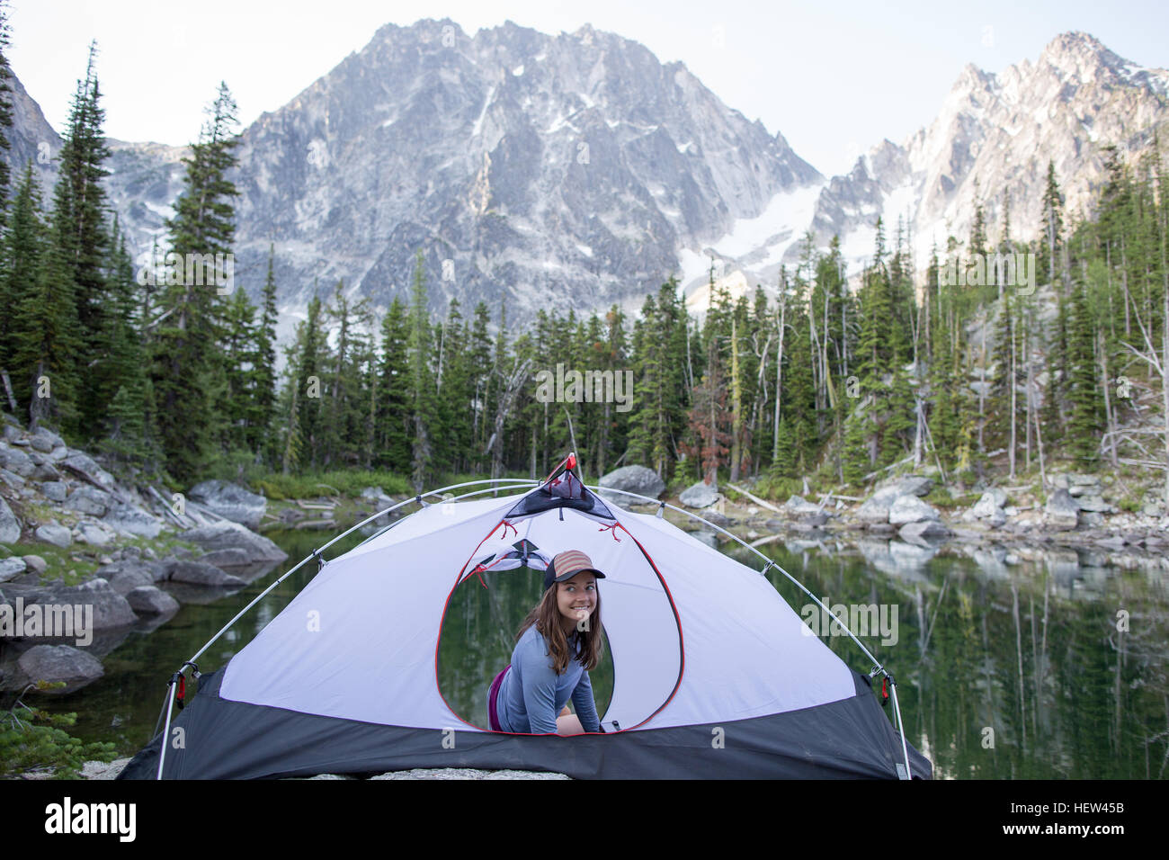 Young woman sitting in tent beside lake, The Enchantments, Alpine Lakes Wilderness, Washington, USA Stock Photo