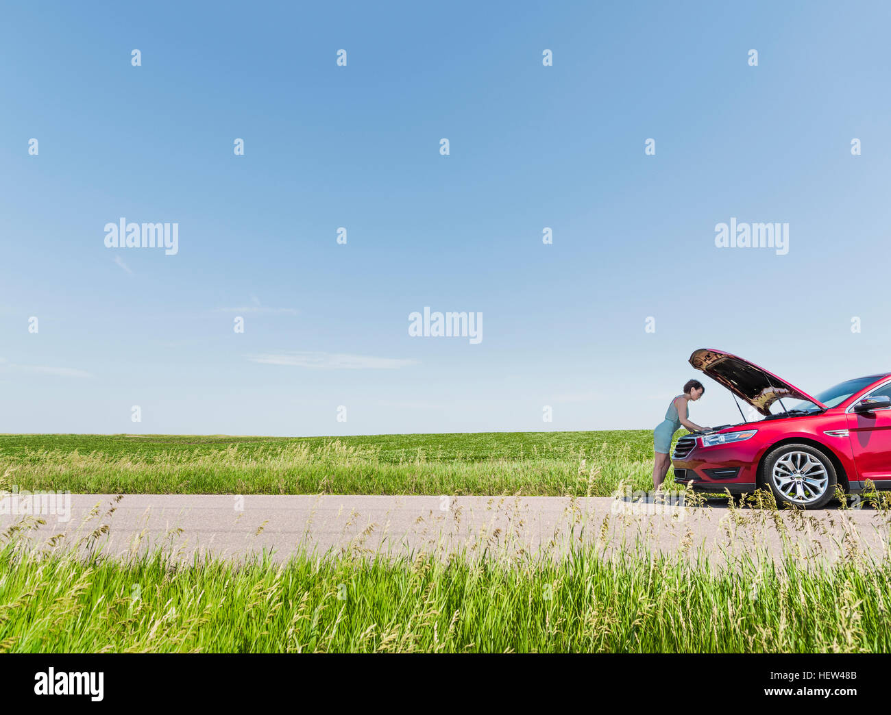 Woman looking under hood of broken down car Stock Photo