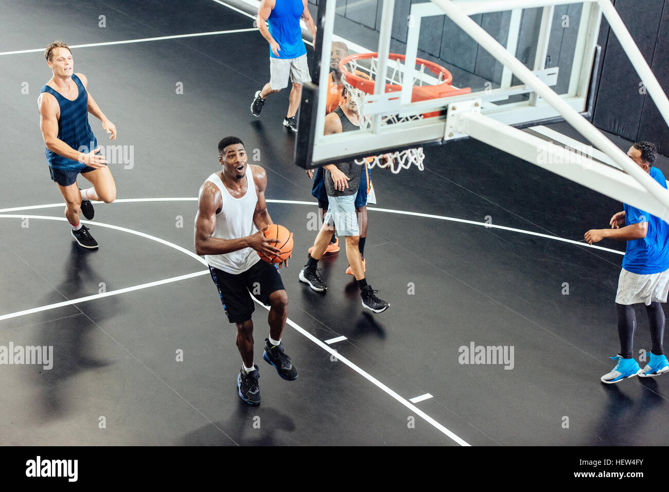 Male basketball team throwing ball into hoop on basketball court Stock
