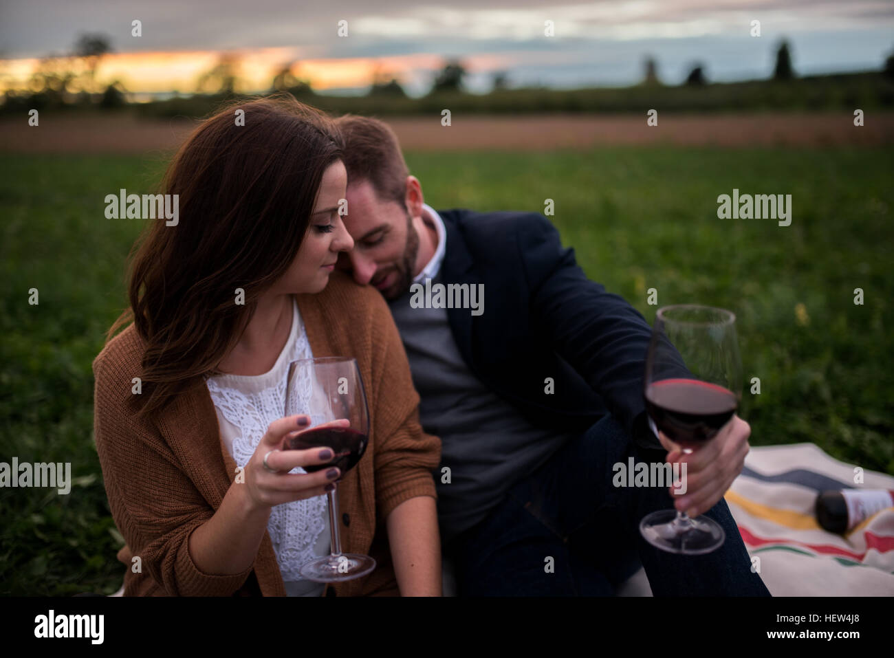 Romantic couple with red wine relaxing on picnic blanket in field at ...