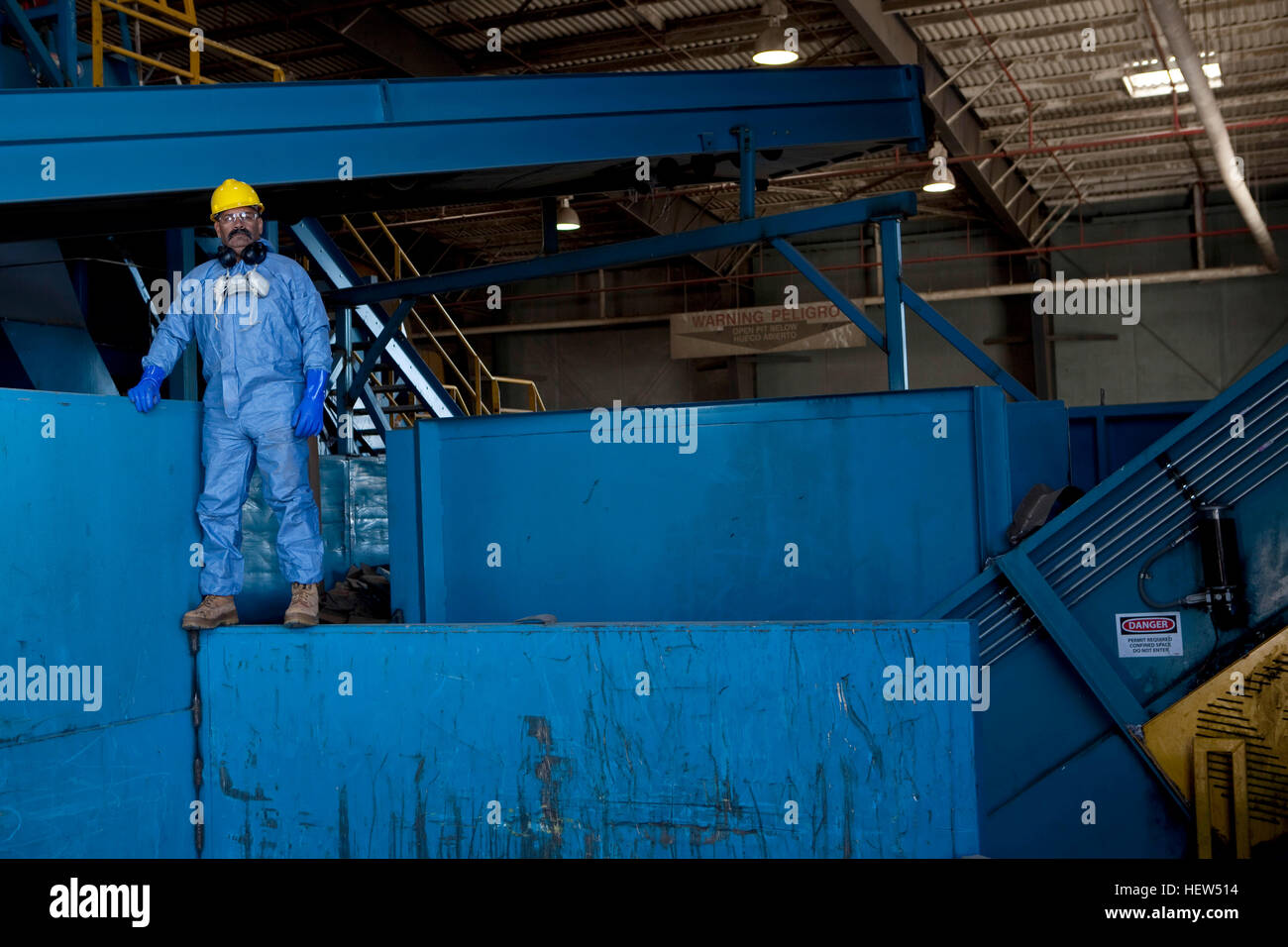 Portrait of male worker in hard hat standing on blue heavy machinery at recycling plant Stock Photo