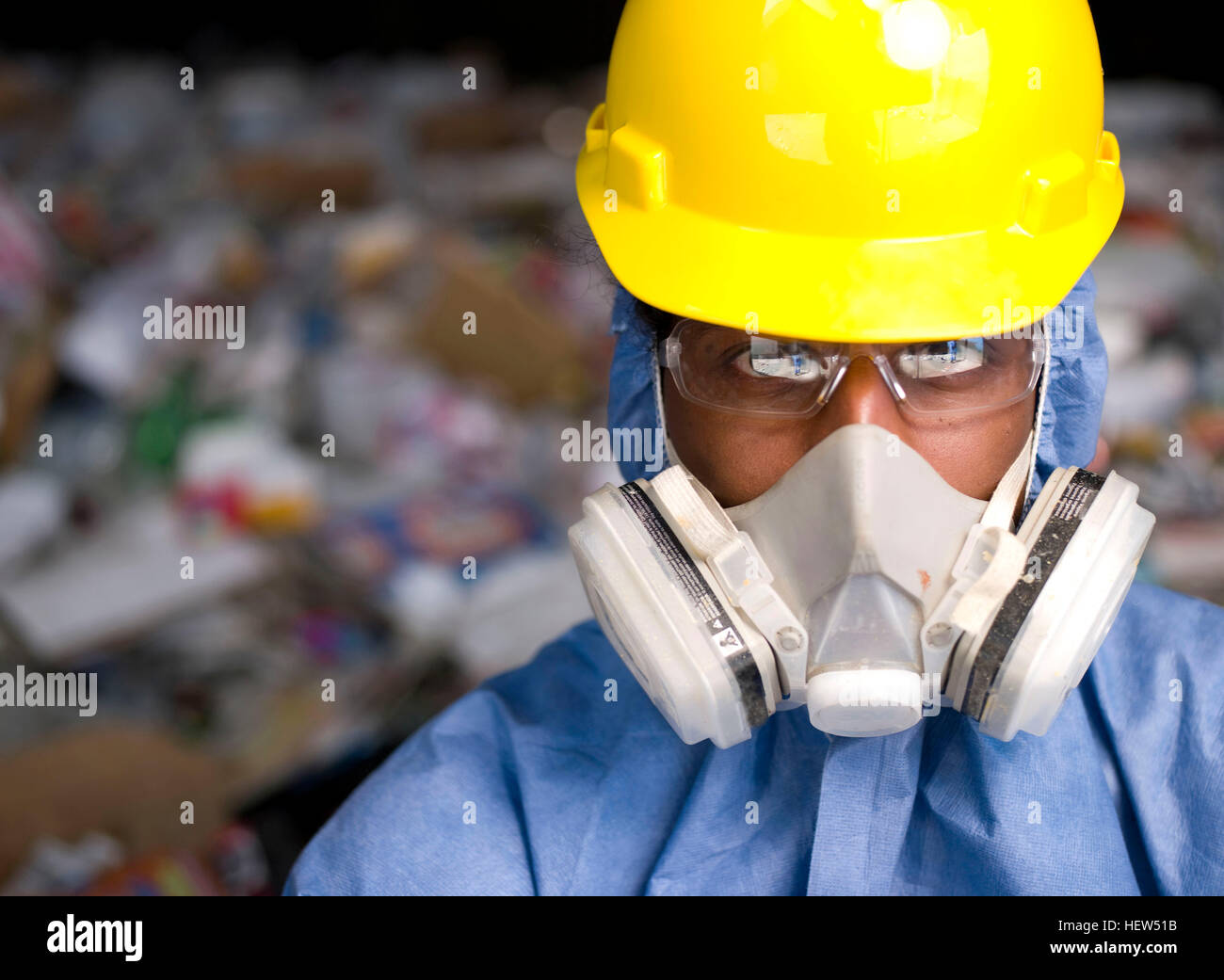 Portrait of male worker in hard hat and gas mask, in front of rubbish at recycling plant Stock Photo