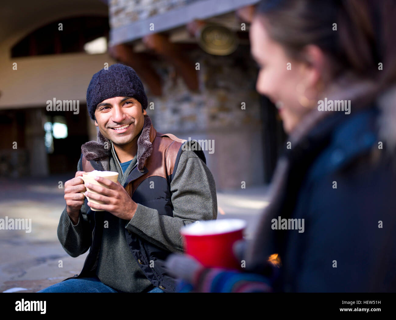 Young couple sitting outside holding hot drinks Stock Photo