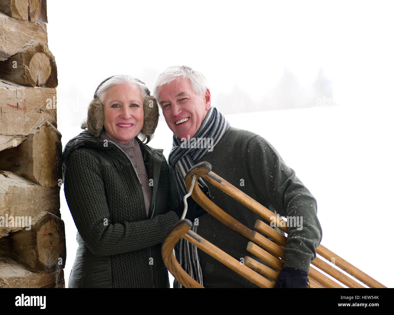 Portrait of couple standing outside cabin in snow carrying toboggan, Colorado, USA Stock Photo