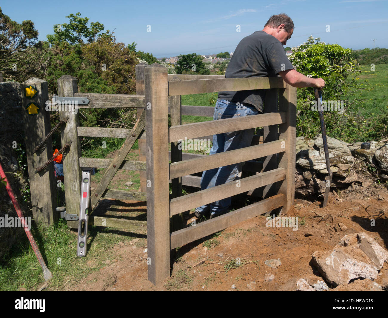 Volunteer replacing corral of wooden kissing gate on public right of way footpath helping less abled to walk Stock Photo