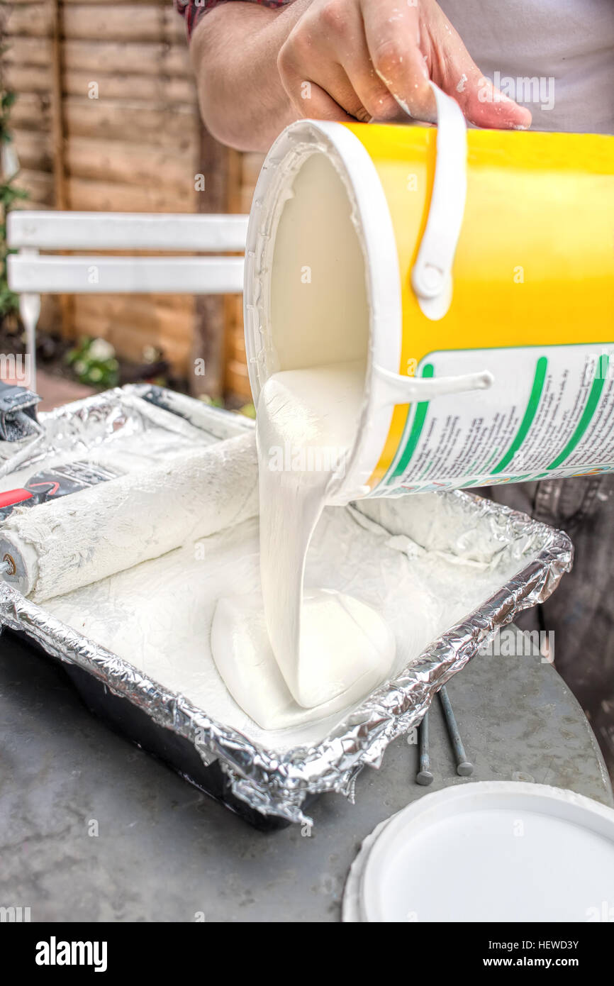 Pouring white paint from tin into tray. DIY home decorating. Stock Photo