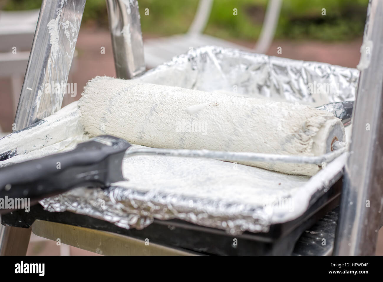 A recently used paint roller in a paint tray with white paint applied ...