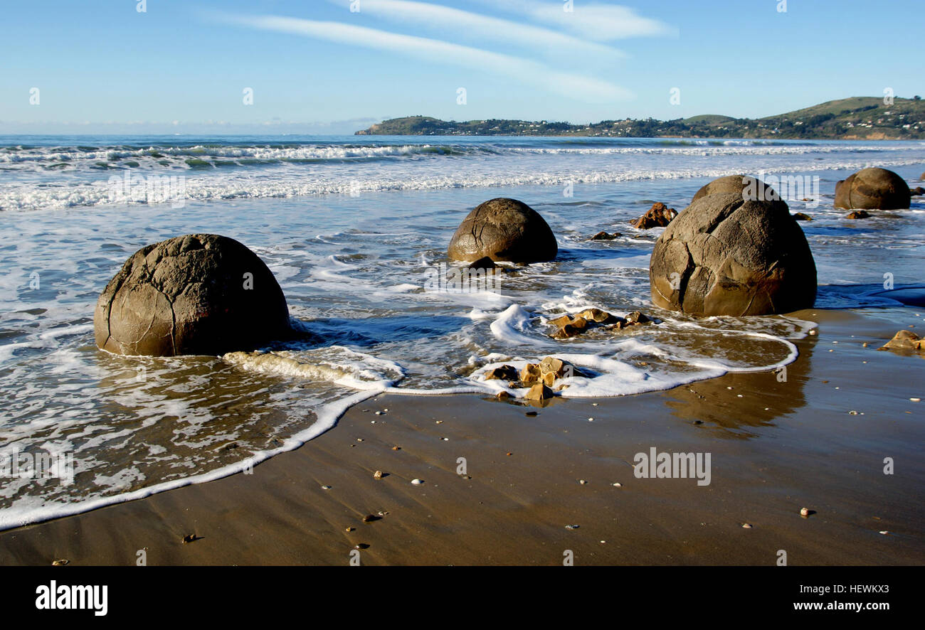 The Moeraki Boulders are unusually large and spherical boulders lying along a stretch of Koekohe Beach on the wave cut Otago coast of New Zealand between Moeraki and Hampden. They occur scattered either as isolated or clusters of boulders within a stretch of beach where they have been protected in a scientific reserve. The erosion by wave action of mudstone, comprising local bedrock and landslides, frequently exposes embedded isolated boulders. These boulders are grey-colored septarian concretions, which have been exhumed from the mudstone enclosing them and concentrated on the beach by coasta Stock Photo