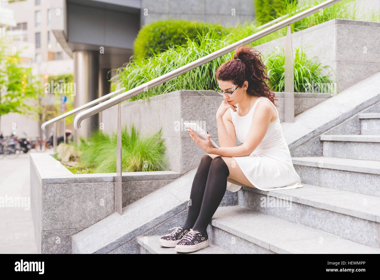 Woman sitting on steps using digital tablet, Milan, Italy Stock Photo ...
