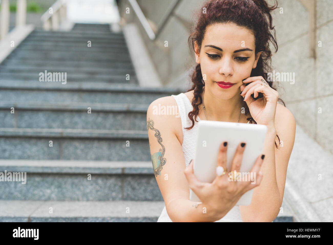 Woman sitting on steps using digital tablet, Milan, Italy Stock Photo ...