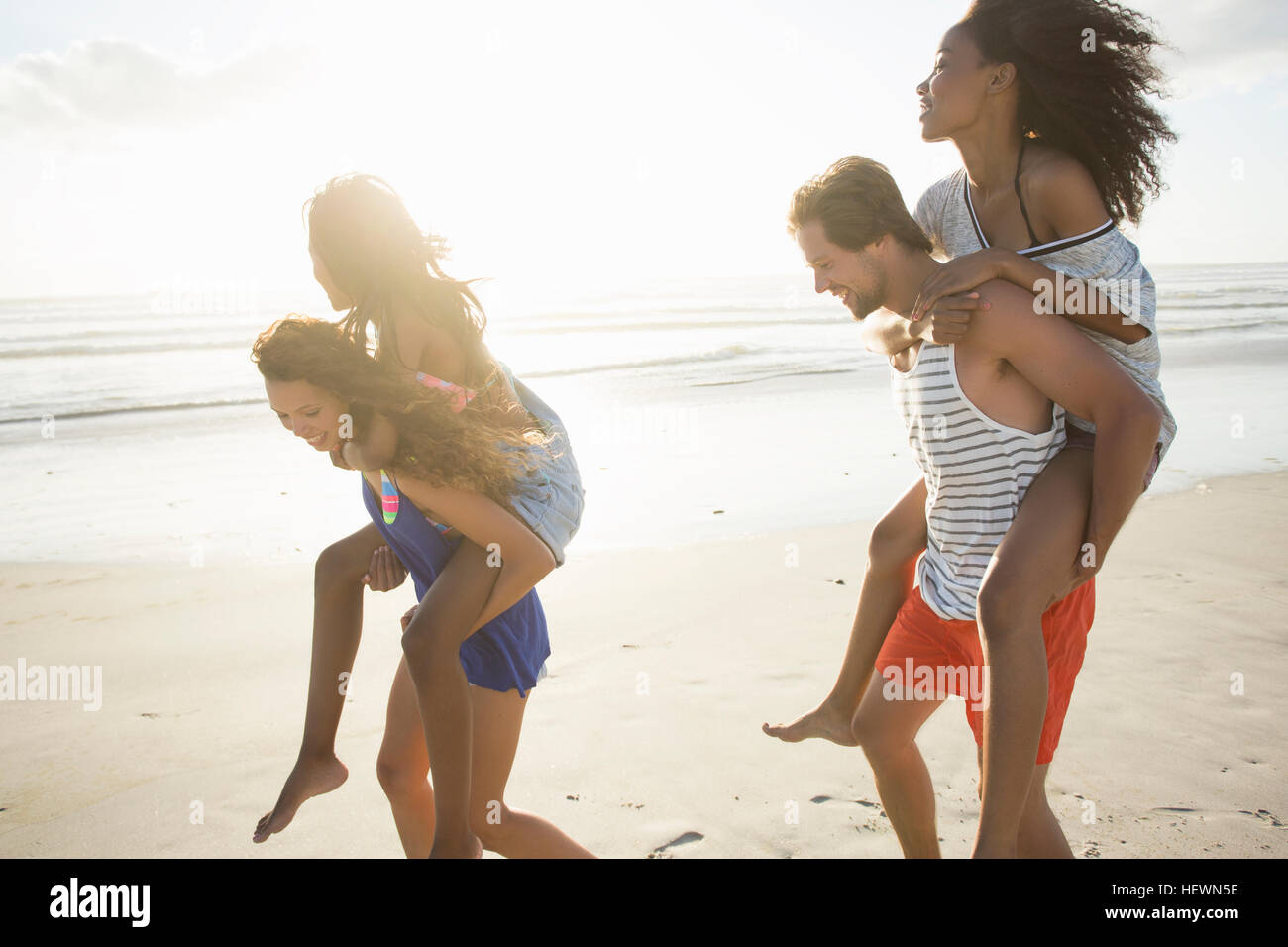 Young man and woman piggybacking friends in beach race, Cape Town, South Africa Stock Photo