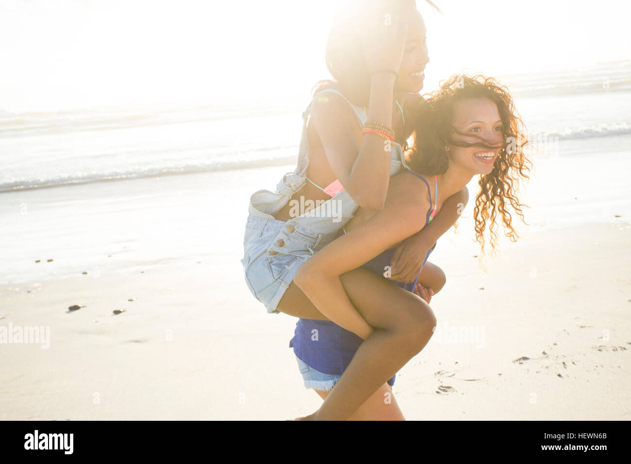 Young woman piggybacking female friend on beach, Cape Town, South Africa Stock Photo