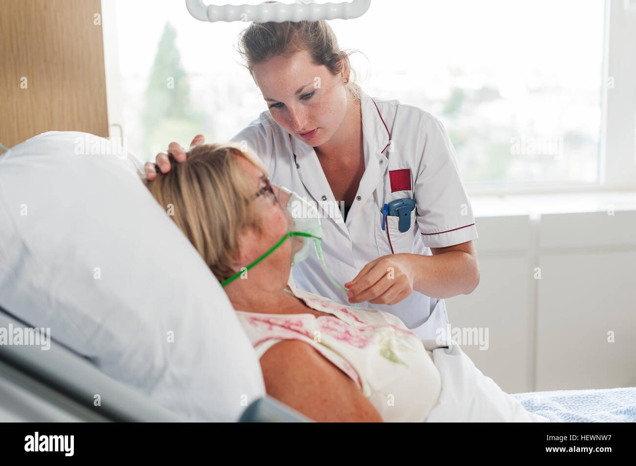 Nurse tending to patient in hospital bed wearing oxygen mask Stock Photo